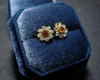 May include: A pair of gold flower-shaped earrings with clear and amber-colored rhinestones, displayed in a blue velvet jewelry box.