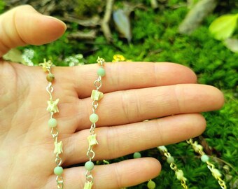 Può includere: Due collane con perline verde chiaro e ciondoli bianchi a forma di osso. Le collane sono su una mano su uno sfondo di muschio verde.