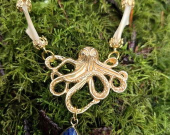 Può includere: Collana con ciondolo a forma di polpo in oro e una goccia di lapislazzuli blu. La collana presenta una delicata catena d'oro e dettagli in osso.