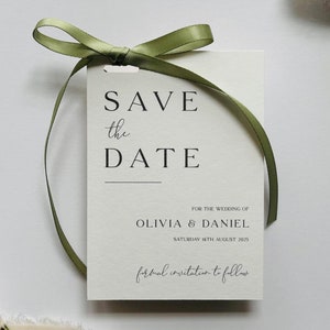 May include: A white Save the Date card with the text "SAVE the DATE" in a minimalist font, tied with a green ribbon. The card includes the names Olivia & Daniel and the date Saturday 16th August 2025.