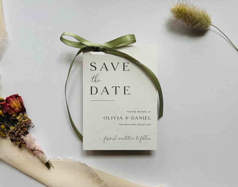 May include: A white Save the Date card with the text "SAVE the DATE" in a minimalist font, tied with a green ribbon. The card includes the names Olivia & Daniel and the date Saturday 16th August 2025.