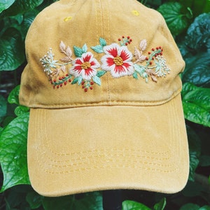 May include: A mustard yellow baseball cap with embroidered floral details in shades of red, white, and green.