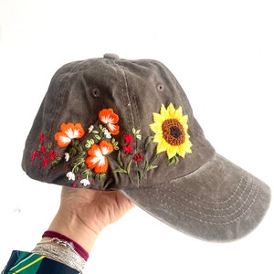 May include: A brown baseball cap with embroidered flowers and a sunflower on the front. The flowers are orange, red, white, and yellow.