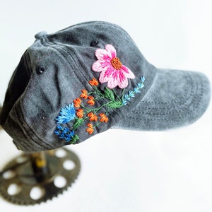 May include: A dark grey baseball cap with a floral embroidery design. The embroidery features pink, orange, blue, and green thread.