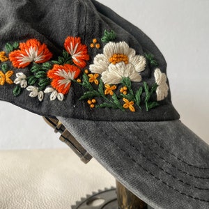 May include: A black baseball cap with a floral embroidery design. The embroidery features orange, white, and green flowers.