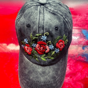 May include: A black denim baseball cap with embroidered red and blue flowers. The cap has a curved brim and a distressed look.