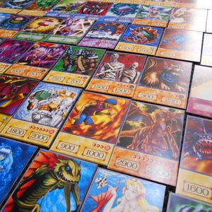 La tua lista di carte Anime (100 carte) include 18 carte rare, una scatola per il mazzo e un tappetino da gioco