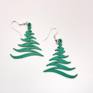 May include: A pair of green Christmas tree earrings with silver-colored ear wires. The earrings are a festive accessory, perfect for the holiday season. The earrings are made of a solid material and have a detailed design.