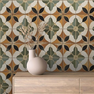 Könnte beinhalten: Eine Wand, die mit dekorativen Keramikfliesen mit einem floralen Muster in Grün-, Braun-, Schwarz- und Weißtönen bedeckt ist. Eine Vase mit abgerundeter Form steht auf einem Holzregal vor der Wand.