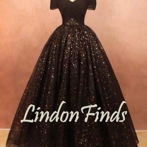 May include: A black off-the-shoulder gown with a full skirt, adorned with gold star-like embellishments. The bodice is fitted, and the skirt flares out. The text "Lindon Finds" is visible on the skirt.