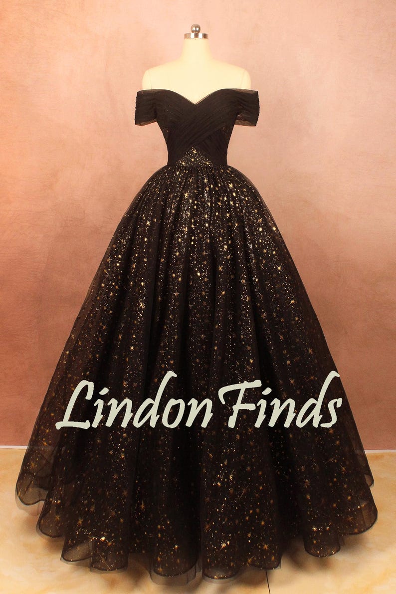May include: A black off-the-shoulder gown with a full skirt, adorned with gold star-like embellishments. The bodice is fitted, and the skirt flares out. The text "Lindon Finds" is visible on the skirt.