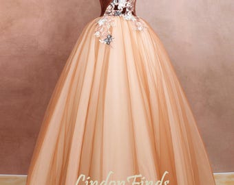 Op de afbeelding: Een bruine en beige off-shoulder baljurk met een fluwelen lijfje en bloemenborduursel. De rok is gemaakt van tule en heeft een volle, vloeiende silhouet. De jurk is perfect voor een formele gelegenheid.