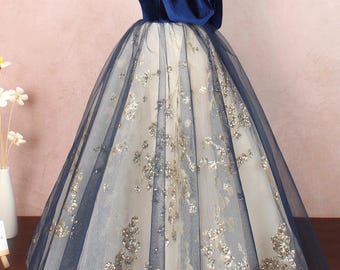 May include: A blue velvet bodice with a tulle skirt featuring gold glitter accents. The skirt is full and flowing, and the bodice has a one-shoulder design.