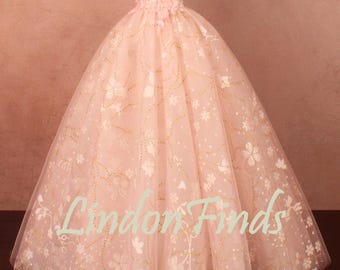 Puede incluir: Un vestido rosa pálido con hombros descubiertos y falda amplia. El vestido presenta detalles florales y dorados, con el texto "Lindon Finds" en la falda. El corpiño tiene un escote corazón.