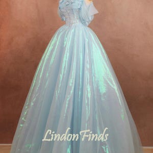 May include: A light blue ball gown with a shimmering, iridescent effect. The strapless bodice is adorned with floral embellishments. The skirt flows to the floor. The text "Lindon Finds" is visible on the skirt.
