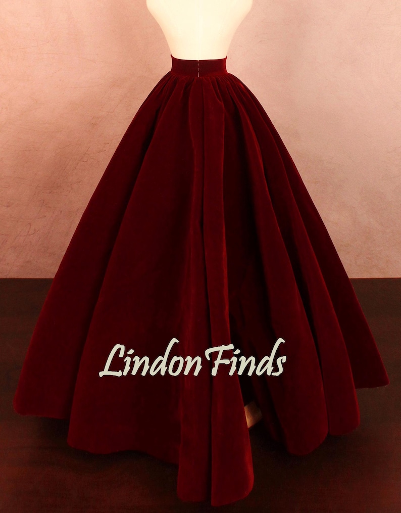 May include: A full, floor-length burgundy velvet skirt on a mannequin. The skirt has a high waist and a wide, flowing silhouette. The text "Lindon Finds" is printed on the skirt.