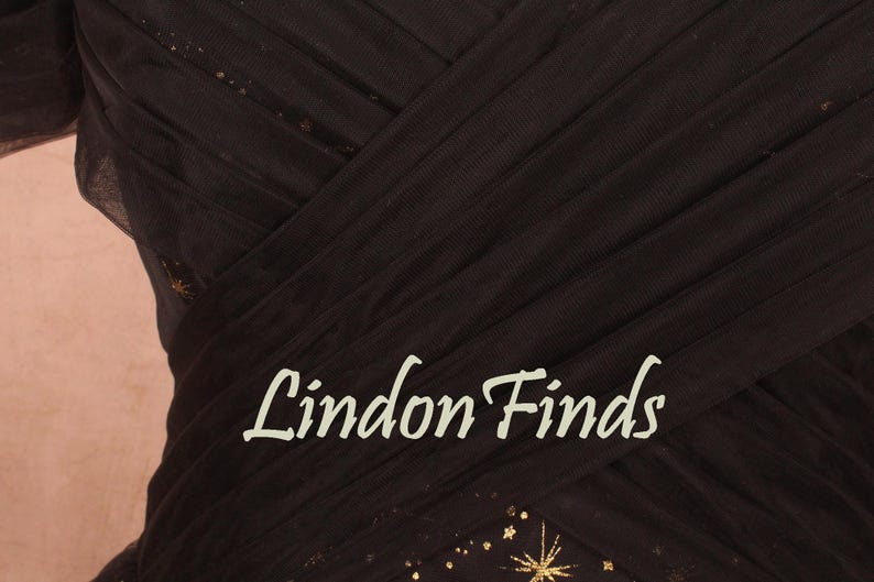 May include: Close-up of a dark brown dress with a layered, pleated design. The dress has a subtle sparkle with gold star accents. The text "Lindon Finds" is displayed in a cursive font.