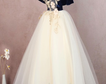 Op de afbeelding: Een formele jurk met een donkerblauw fluwelen lijfje en een witte tule rok. Het lijfje heeft een sweetheart-halslijn en off-the-shoulder bandjes. De rok is vol en zwierig. Het lijfje is versierd met bloemenborduurwerk.