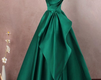 May include: A strapless emerald green satin ball gown with a fitted bodice and a flowing skirt. The skirt has a unique design with a layered, asymmetrical ruffle.