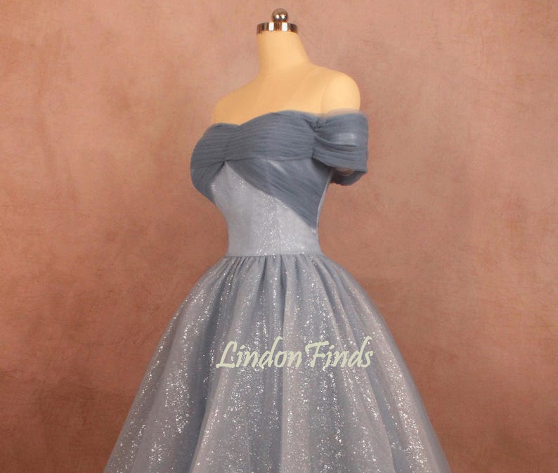 K&ouml;nnte beinhalten: Ein hellblaues, schulterfreies Kleid mit einem glitzernden T&uuml;llrock. Das Oberteil hat ein mehrlagiges T&uuml;lldesign und eine figurbetonte Silhouette. Das Kleid wird auf einer Schaufensterpuppe vor einem braunen Hintergrund gezeigt. Der Text "Lindon Finds" ist auf dem Rock sichtbar.