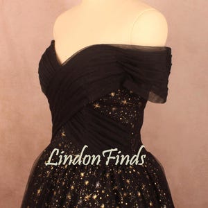 May include: A black off-the-shoulder dress with a bodice and skirt adorned with gold star patterns. The dress features a layered, pleated design and the text "Lindon Finds" in a cursive font.