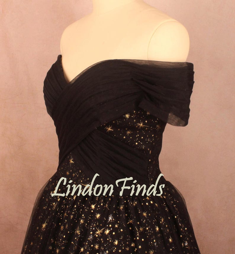 May include: A black off-the-shoulder dress with a bodice and skirt adorned with gold star patterns. The dress features a layered, pleated design and the text "Lindon Finds" in a cursive font.