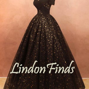 May include: A black off-the-shoulder gown with a full skirt, adorned with gold star-shaped embellishments. The dress is displayed on a mannequin. The text "Lindon Finds" is visible on the skirt.