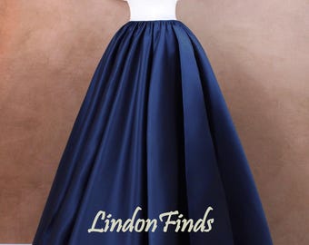 Op de afbeelding: Een wit off-shoulder top met een gerimpelde halslijn en een donkerblauwe satijnen rok. De rok is vol en zwierig, en de jurk is perfect voor een formele gelegenheid. De jurk is op een mannequin en de tekst "Lindon Finds" is zichtbaar op de rok.