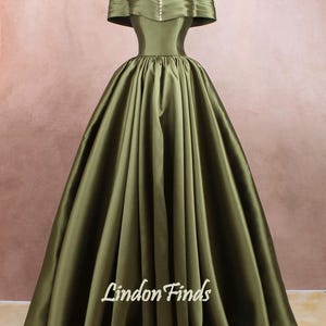 May include: A long, flowing, off-the-shoulder green satin gown with a fitted bodice and a full skirt. The gown has a simple design with a row of small buttons down the front of the bodice. The gown is perfect for a formal event.