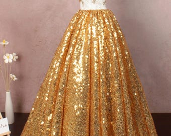 Op de afbeelding: Een gouden pailletten baljurk met een witte off-shoulder bodice. De jurk heeft een volle rok en is perfect voor een formele gelegenheid.