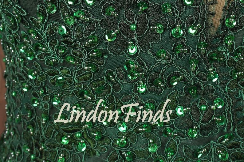 Op de afbeelding: Close-up van een donkergroene stof met ingewikkeld bloemenkant en glinsterende groene pailletten. De tekst "Lindon Finds" staat in een cursief lettertype over de stof. Het ontwerp is gedetailleerd en elegant.