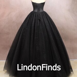May include: A black strapless ball gown with a fitted bodice and a full skirt. The skirt is made of tulle and has a sparkly finish. The gown is cinched at the waist with a satin ribbon.