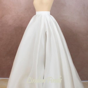 May include: A white satin skirt with a front slit. The skirt is full and flowing, and it is being displayed on a mannequin.
