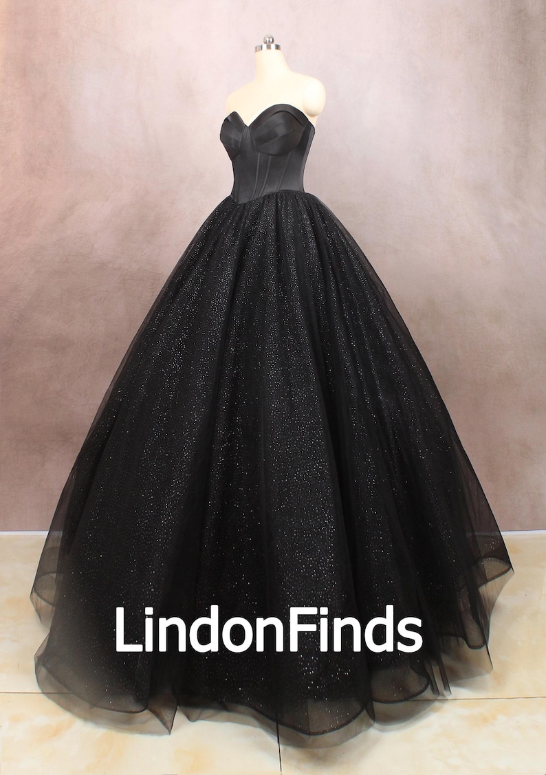 May include: A black strapless ball gown with a sparkling tulle skirt. The bodice is fitted and has a sweetheart neckline. The skirt is full and flowing. The dress is perfect for a formal event.