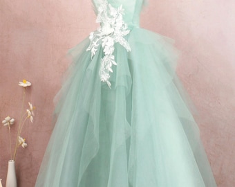 May include: A mint green tulle ball gown with a white lace applique and feather trim. The dress is on a mannequin and has a layered skirt.