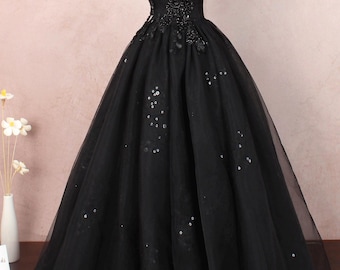 May include: A black ball gown with a sweetheart neckline and off-the-shoulder sleeves. The bodice is embellished with intricate beadwork, and the skirt features scattered sequins. The dress is displayed on a mannequin.