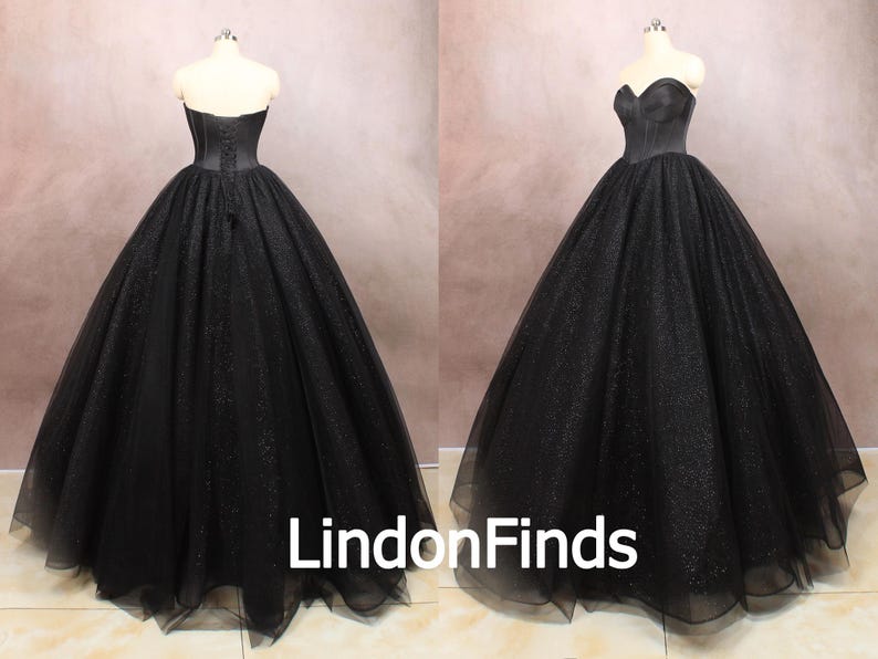 May include: A black strapless ball gown with a fitted bodice and a full skirt. The skirt is made of tulle and has a sparkly finish.