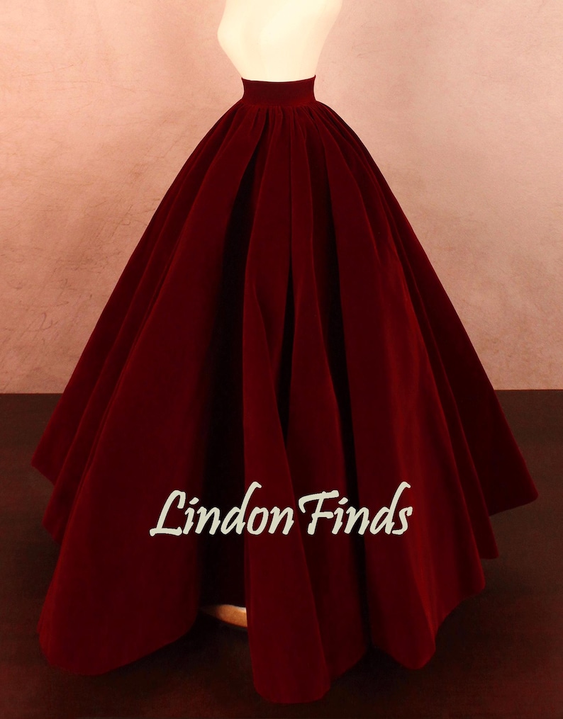 May include: A full, floor-length burgundy velvet skirt. The skirt has a high waist and is gathered at the waistline, creating a voluminous silhouette. The text "Lindon Finds" is printed on the skirt.