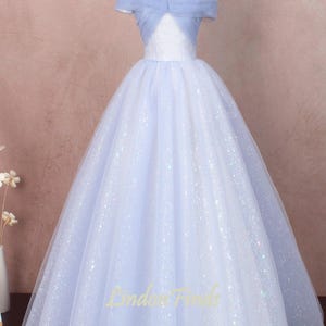 K&ouml;nnte beinhalten: Ein hellblaues T&uuml;ll-Ballkleid mit einem glitzernden, schillernden Finish. Das Kleid hat einen Off-Shoulder-Ausschnitt und ein tailliertes Oberteil.
