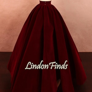 May include: A full, floor-length burgundy velvet skirt displayed on a mannequin. The skirt has a high waist and a voluminous silhouette. The text "Lindon Finds" is printed on the skirt.