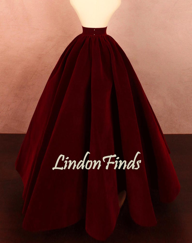 May include: A full, floor-length burgundy velvet skirt displayed on a mannequin. The skirt has a high waist and a voluminous silhouette. The text "Lindon Finds" is printed on the skirt.