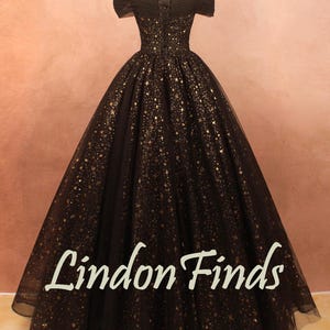 May include: A black off-the-shoulder gown with gold star-like embellishments. The dress features a fitted bodice and a full, flowing skirt. The text "Lindon Finds" is visible on the skirt.
