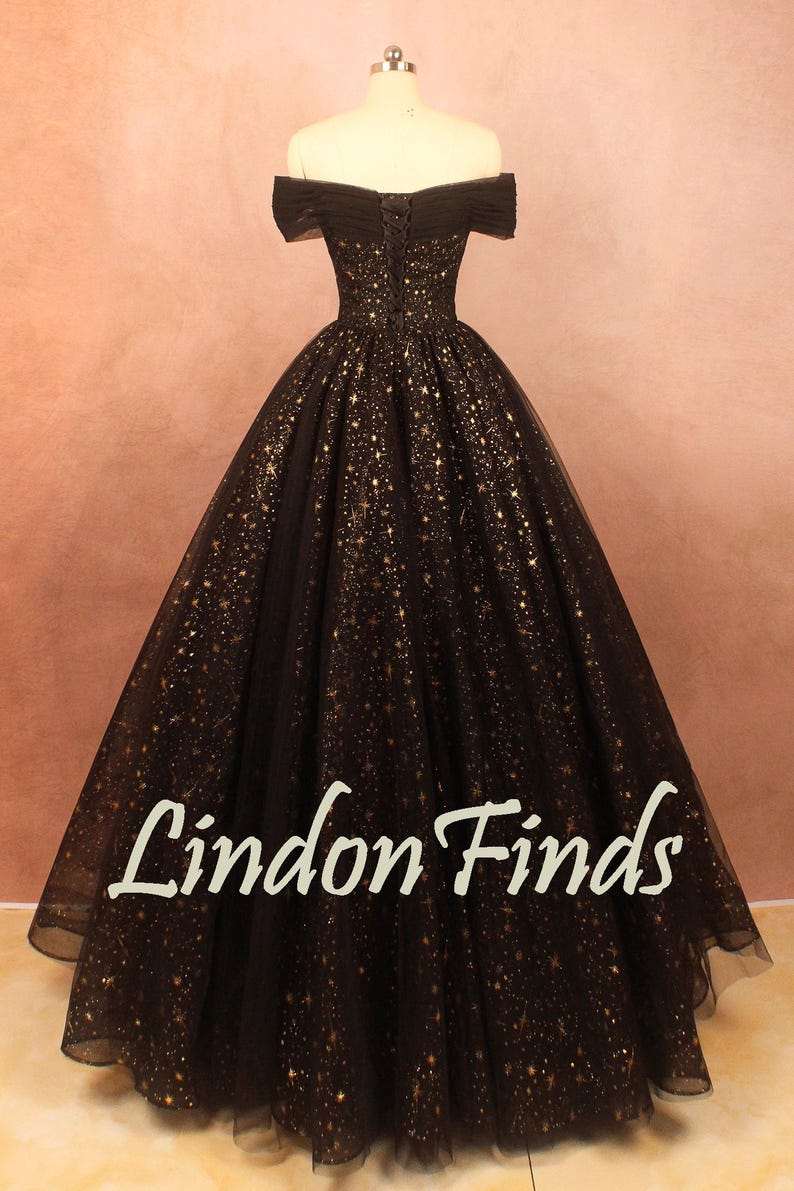 May include: A black off-the-shoulder gown with gold star-like embellishments. The dress features a fitted bodice and a full, flowing skirt. The text "Lindon Finds" is visible on the skirt.