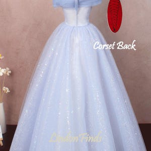 K&ouml;nnte beinhalten: Ein hellblaues T&uuml;ll-Ballkleid mit herzf&ouml;rmigem Ausschnitt und schulterfreien Tr&auml;gern. Das Kleid ist mit schimmerndem Glitzer bedeckt und hat einen Korsett-R&uuml;cken.