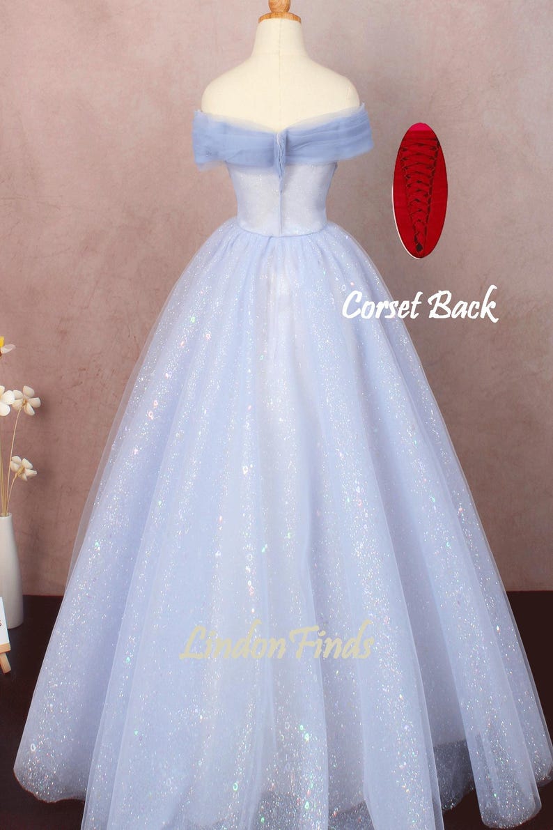 K&ouml;nnte beinhalten: Ein hellblaues T&uuml;ll-Ballkleid mit herzf&ouml;rmigem Ausschnitt und schulterfreien Tr&auml;gern. Das Kleid ist mit schimmerndem Glitzer bedeckt und hat einen Korsett-R&uuml;cken.
