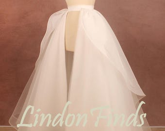 May include: A white tulle overskirt featuring a high-low hemline and a structured waistband, displayed on a mannequin. The sheer, layered fabric creates a voluminous silhouette with an open front design. The text Lindon Finds is visible.