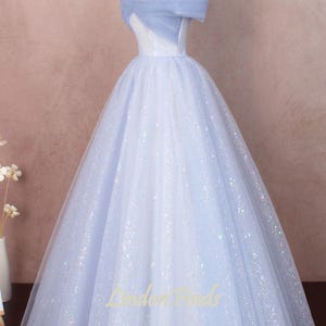 K&ouml;nnte beinhalten: Ein hellblaues, schulterfreies Ballkleid mit einem T&uuml;ll-Oberteil und einem glitzernden T&uuml;llrock. Das Kleid hat ein tailliertes Oberteil und einen vollen Rock.