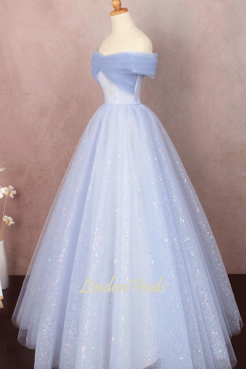 K&ouml;nnte beinhalten: Ein hellblaues, schulterfreies Ballkleid mit einem T&uuml;ll-Oberteil und einem glitzernden T&uuml;llrock. Das Kleid hat ein tailliertes Oberteil und einen vollen Rock.
