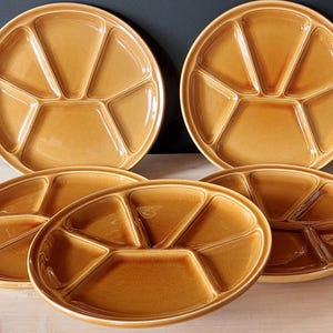 Può includere: Un gruppo di sei piatti da portata in ceramica color beige. Ogni piatto è diviso in sei sezioni triangolari, ideali per servire antipasti o snack. I piatti hanno una finitura lucida e sono disposti su una superficie di legno chiaro.
