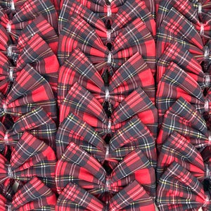 May include: A close-up of a stack of red and black tartan bows. The bows are made of fabric and have a ruffled texture.